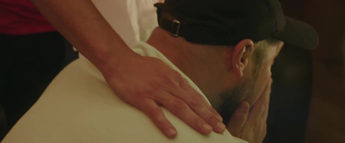 Standing man pats shoulder of man sitting and crying