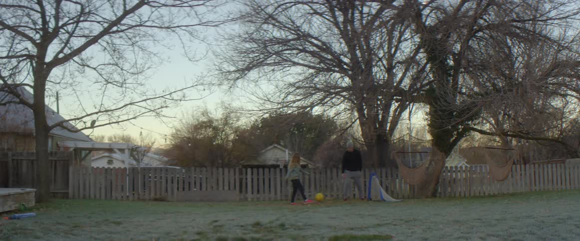 A little girl kicks a soccer ball into a net in the yard as she plays with dad