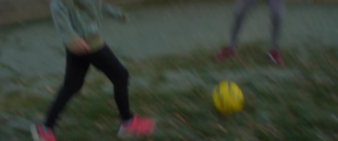 A girl kicks a ball outside into a small soccer net