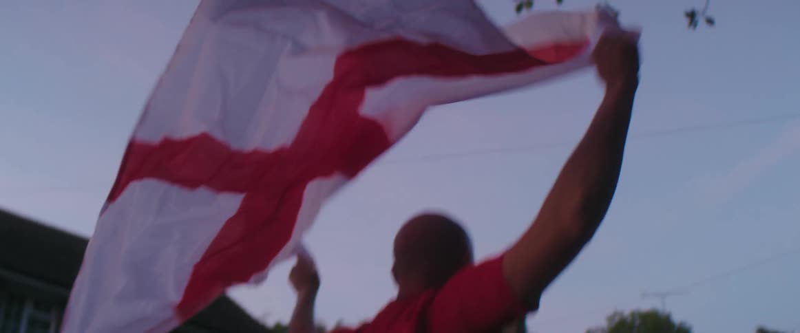 A man holds a flag over his head and cheers as he walks down a street