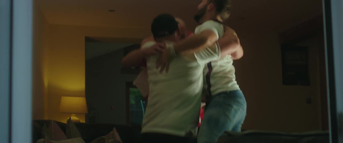 Men watching sports on television jump and hug in celebration