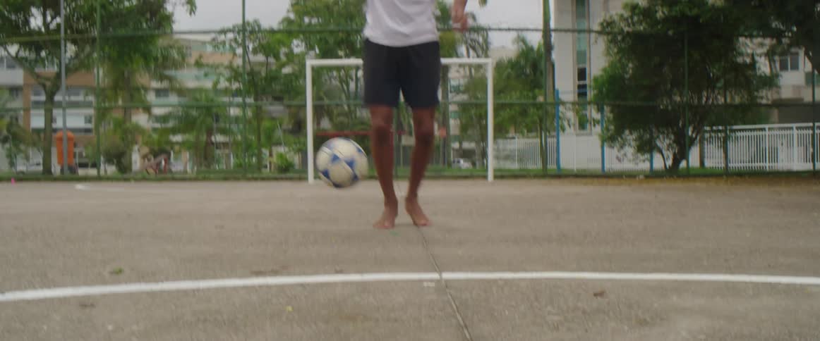 Youth throws soccer into air before dribbling it across pavement