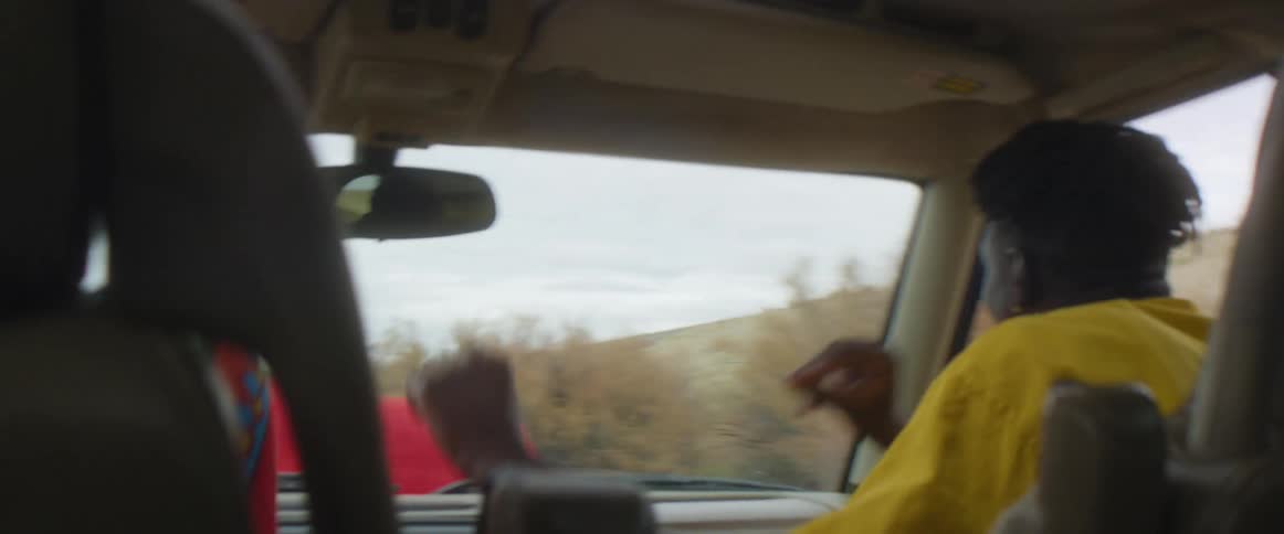 A man dances in the front passenger seat of a car driving in a rural area