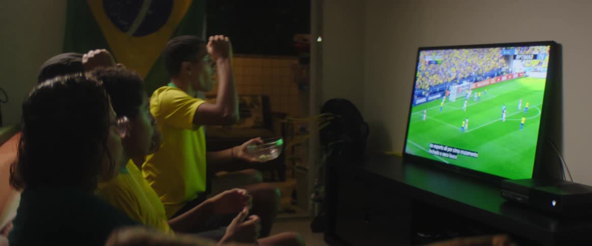 Father mother and sons wearing brazilian football uniform watch football match on television in living room at home
