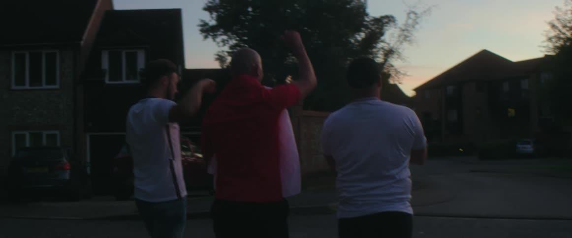 Three men walk through a neighborhood raising their fists in celebration