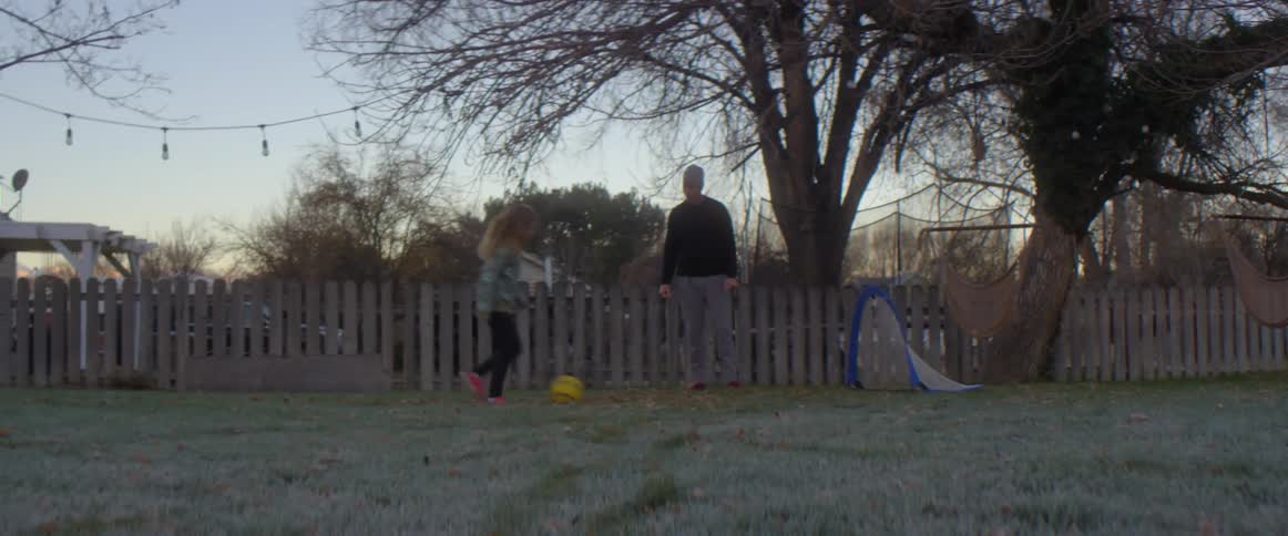 Little girl kicks ball across yard and into a goal with an older man