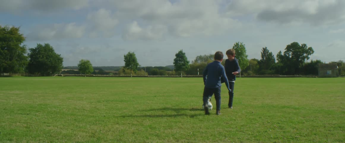 Two boys play with a soccer ball on a grass field in a park