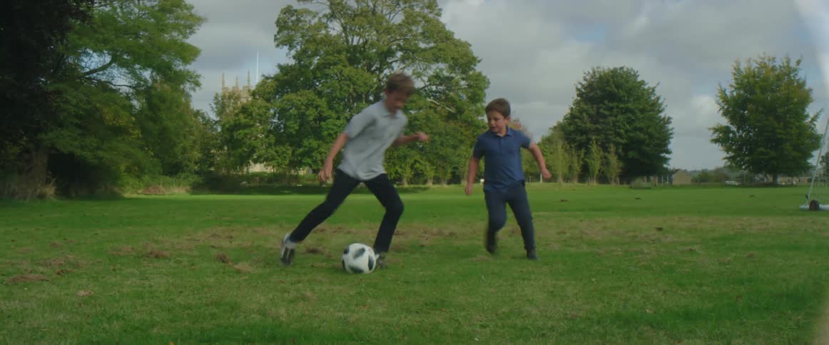 A boy kicks a soccer ball into the net while playing with a friend