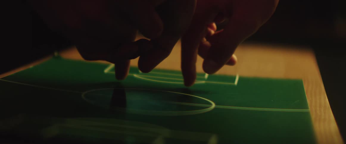 Two people run their fingers along a piece of paper with a field and goal drawn on it