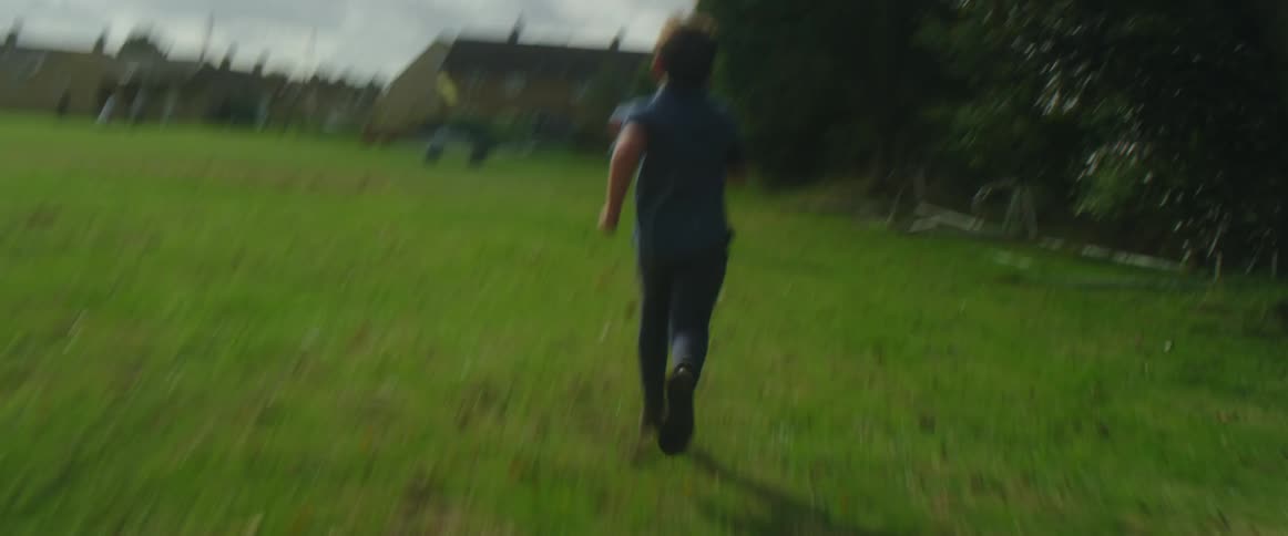 A boy chases his brother as he runs kicking a soccer ball on a grass field