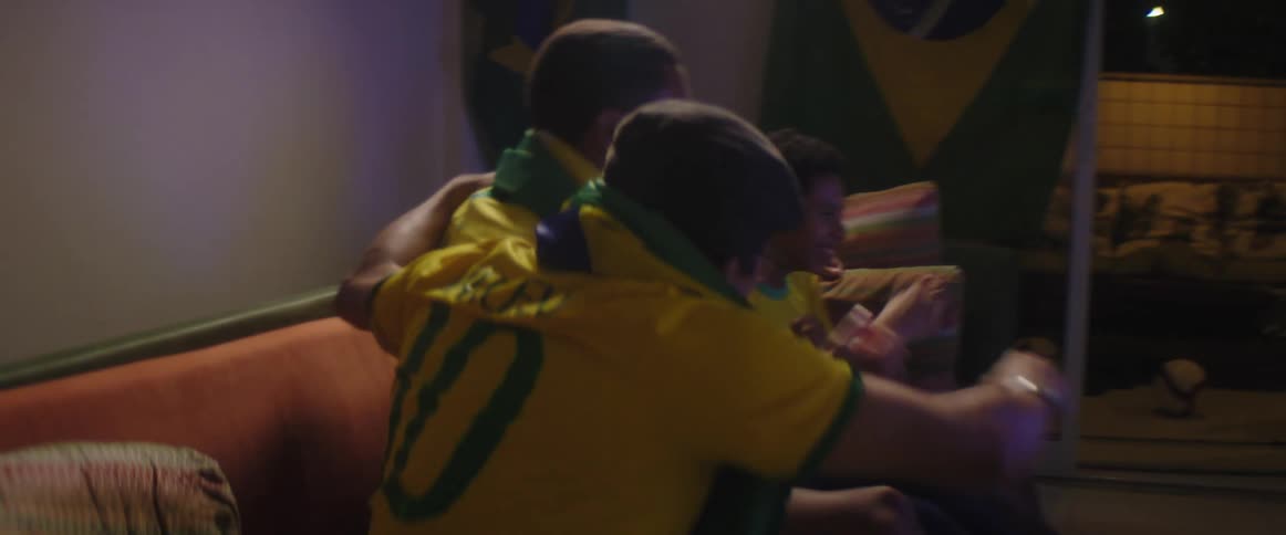 Father mother and sons wearing brazilian football uniform watch football match on television in living room at home