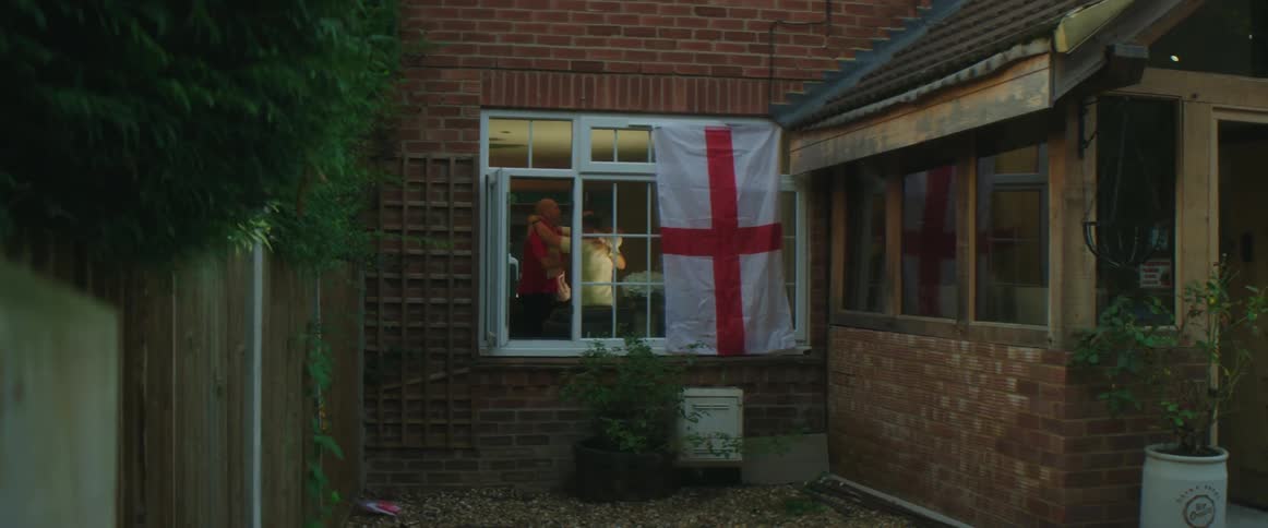 British fans watching football on television celebrate goal seen outside of house with england flag hanging on window