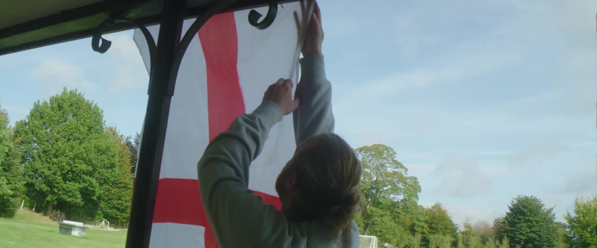 A man hangs a flag in a park with a goal post set up