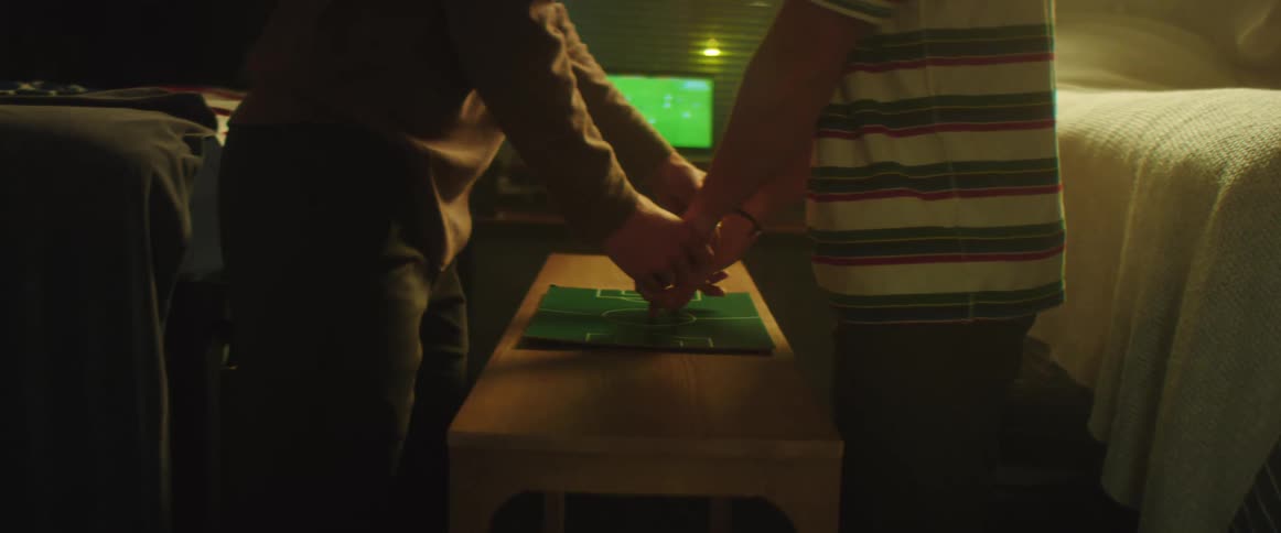 A man guides a younger mans fingers over a small soccer field mat and they jump for joy and hug