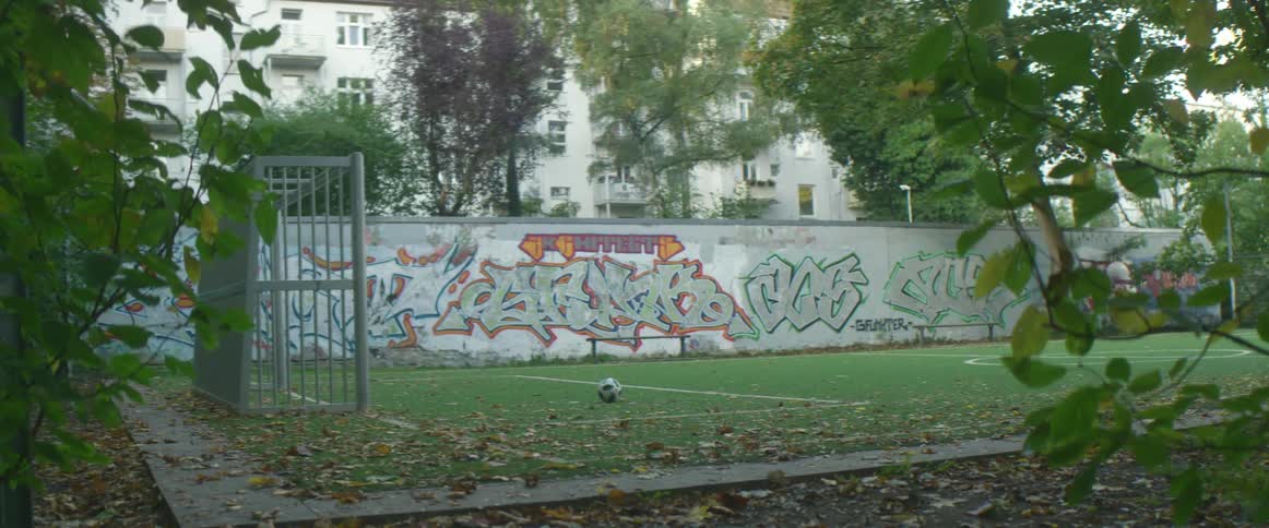 A soccer ball sitting on a soccer field surrounded by graffitied walls in a city