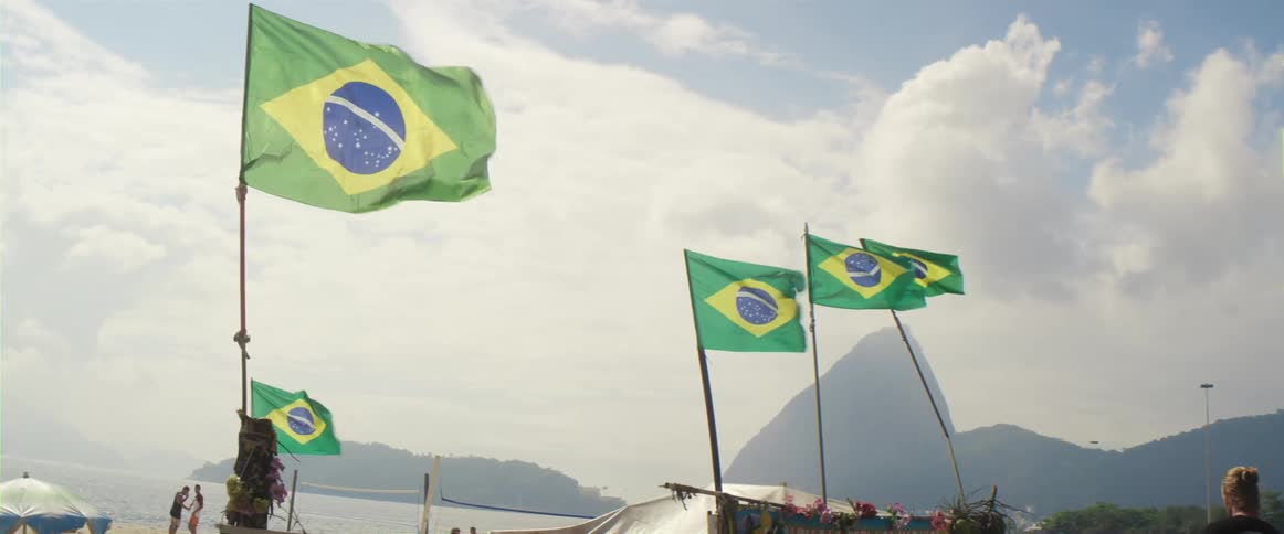 Brazilian flags are flying in strong wind under a cloudy sky