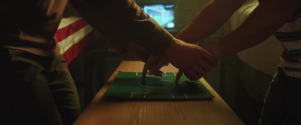 One person guides another persons hands on small game field map sitting on wooden surface