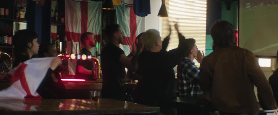 People in a crowded bar cheer as they watch a soccer game on a projector screen
