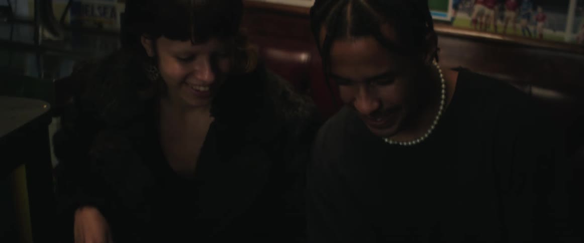 A man and woman sit on a couch and talk as they look at a cell phone and then cheer