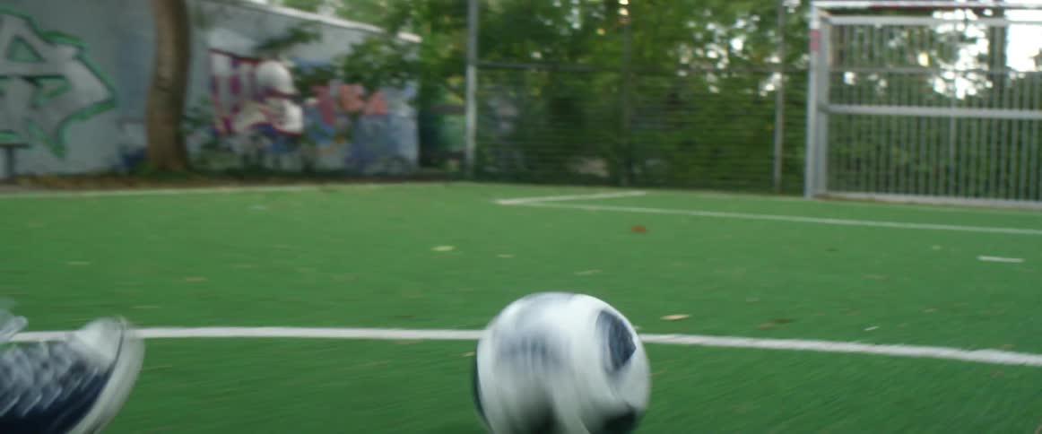 A soccer ball being kicked across an outdoor field and into a goal