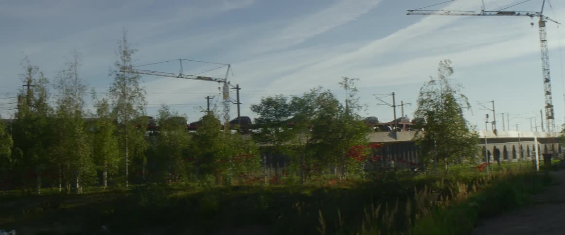 A freight train carrying cars passes through a city atop a bridge during the day