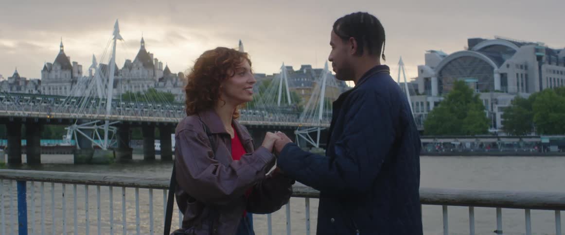 Man and woman are holding hands on a bridge at dusk
