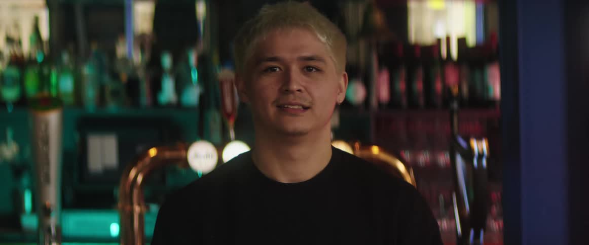 A bartender smiles as he poses behind the bar in front of a wall of liquor bottles