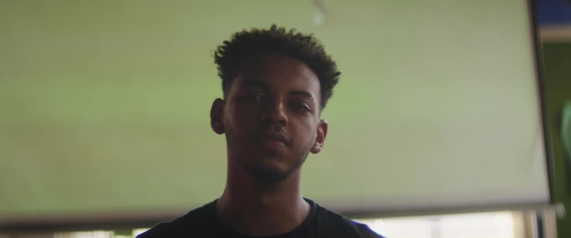 Teenage boy stands in front of television with football match on and looks at the camera
