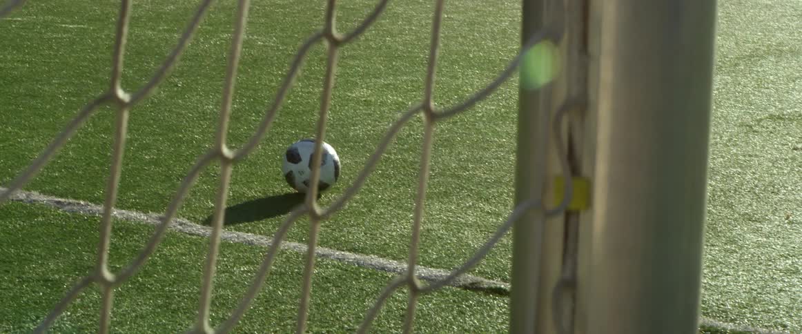 A soccer ball is left on en empty field outdoors
