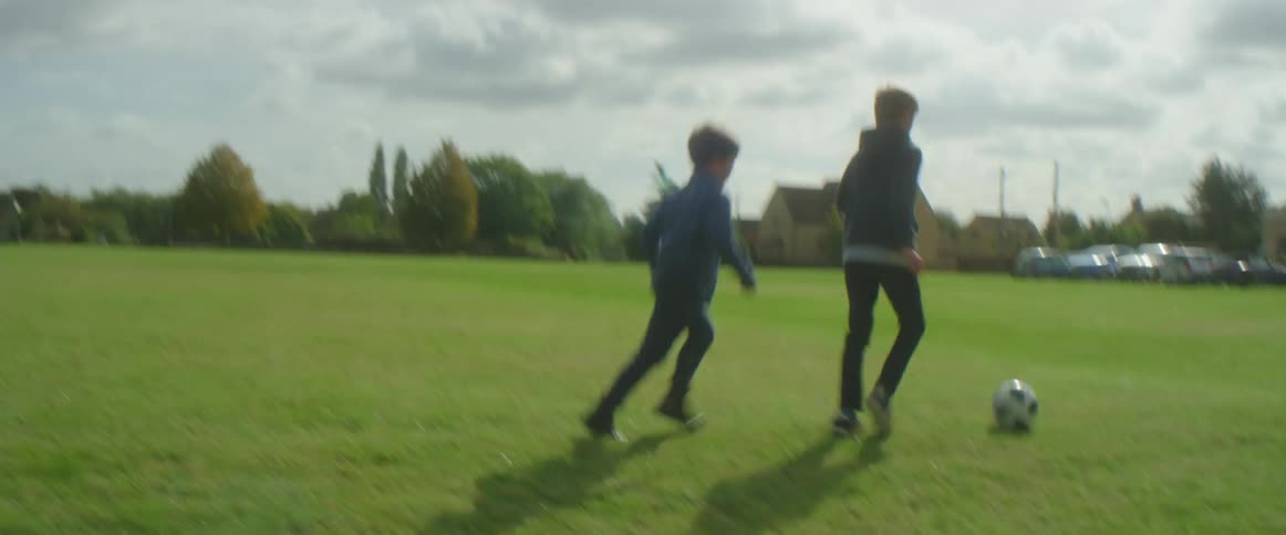 Two boys play soccer together in a large outdoor space
