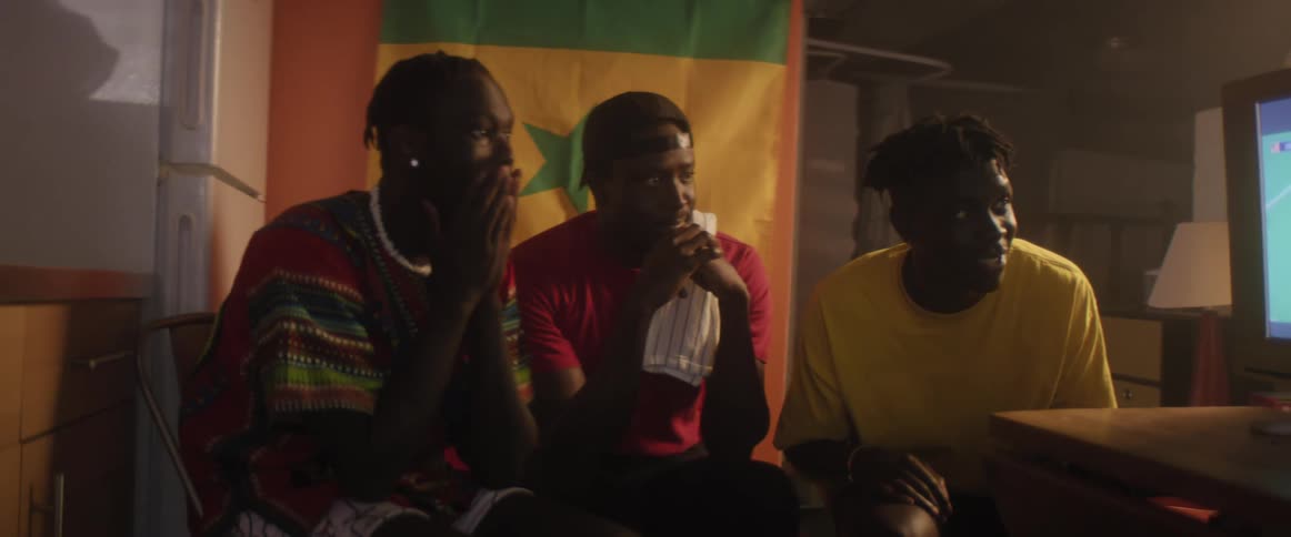 Three men cheer as they watch a soccer match on tv
