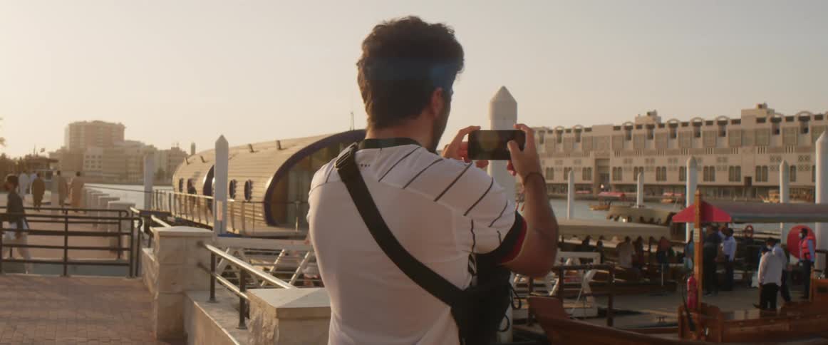 Young man takes pictures of the waterfront city with his phone at sunset