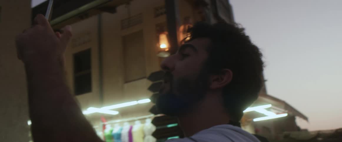 A man holds his smartphone up to better see the screen as he uses it outdoors in the evening