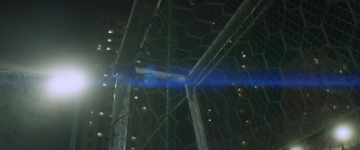 A bright light shining down on a soccer net on an outdoor field at night
