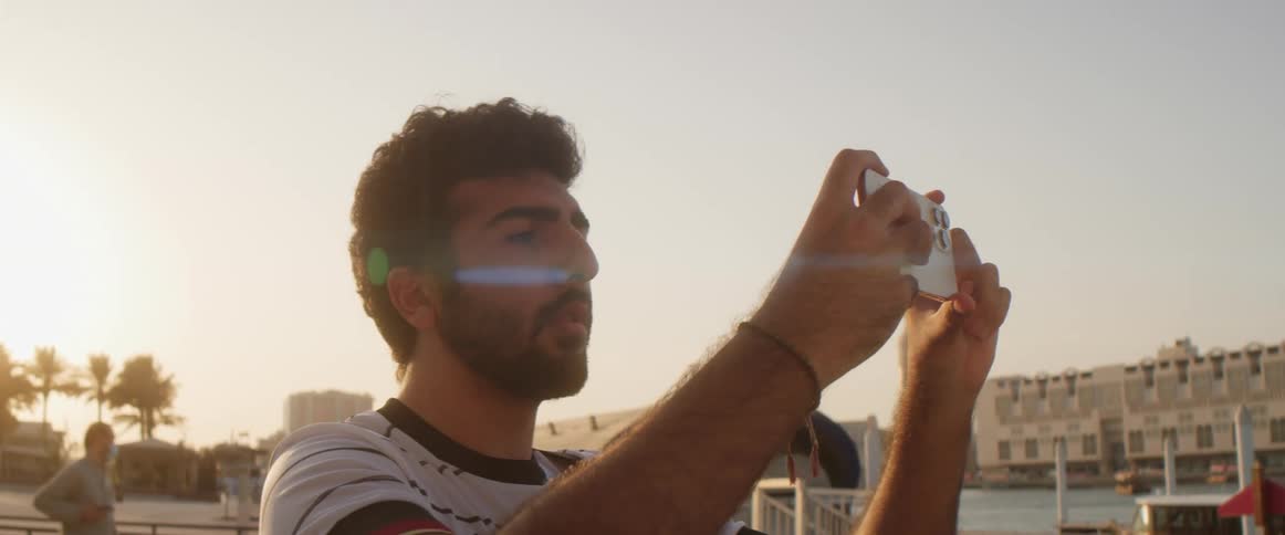 Man standing near with river and boat in background takes picture with a smartphone