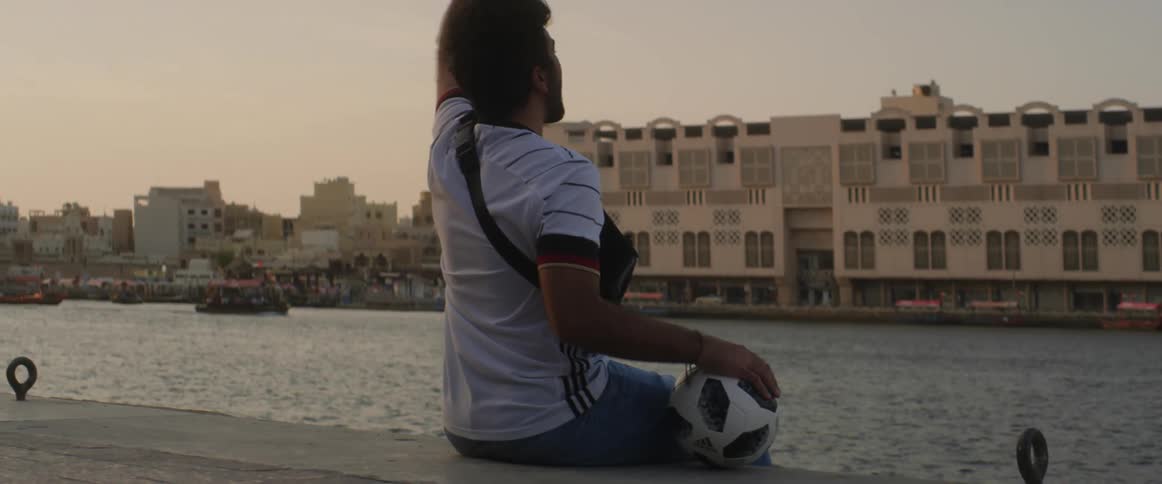 A man is sitting next to a river in a city and pumps his fist in the air while smiling