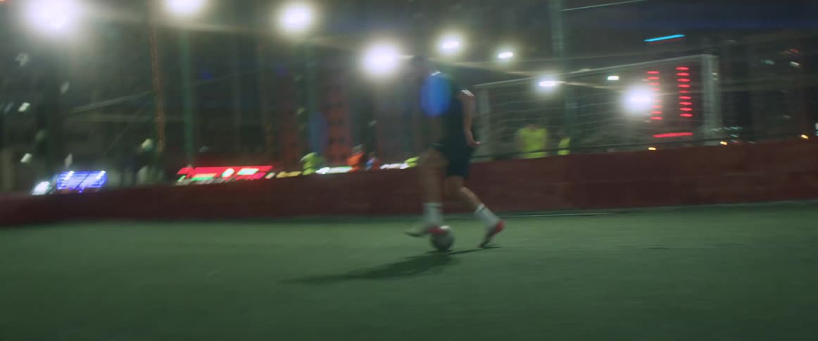 A man kicks a soccer ball quickly across an outdoor rooftop field