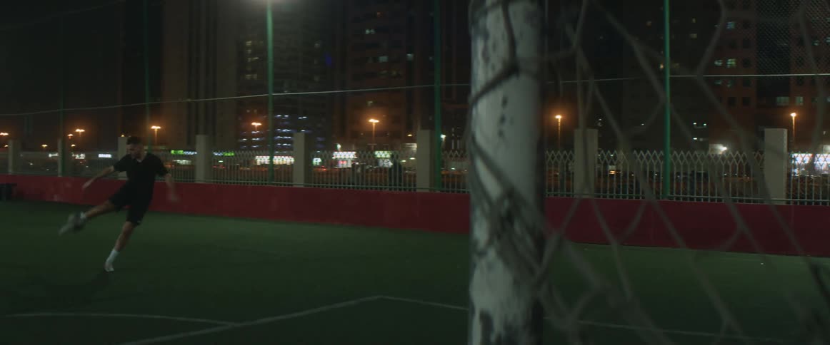 A man kicks a soccer ball around at night