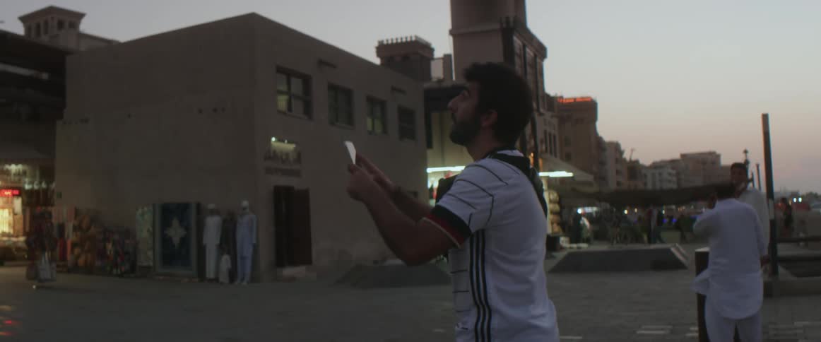 A man traveling in a remote village stops and takes a picture of shops with his cell phone