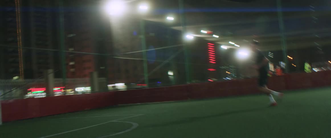 Young man practicing soccer on a soccer field in the city at night