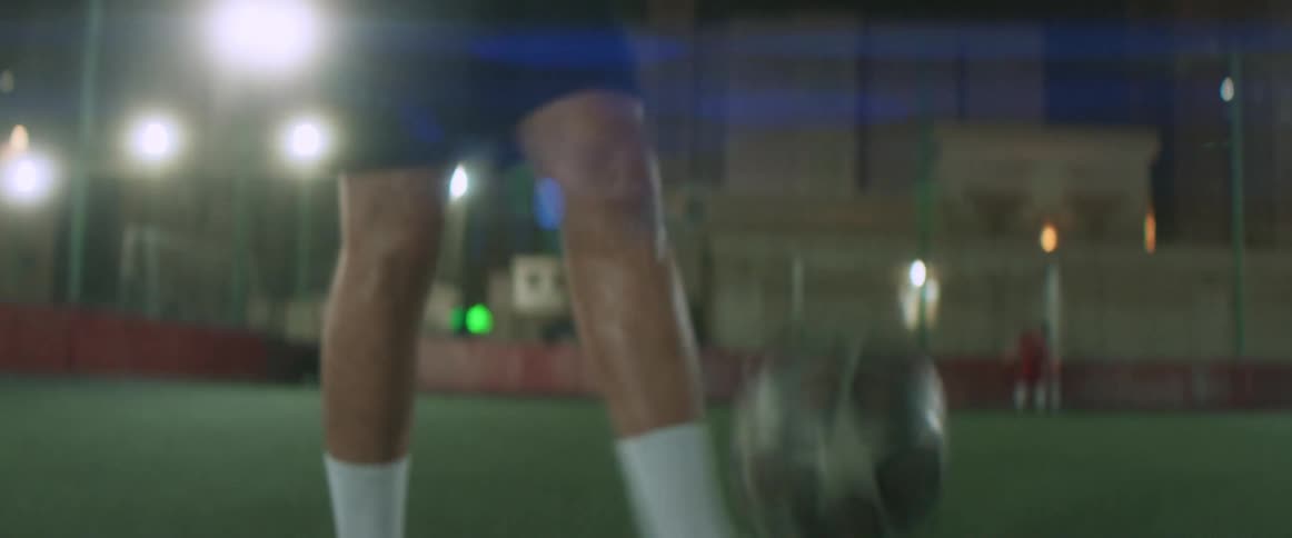 Male athlete practices with soccer ball standing on turf covered soccer field at night