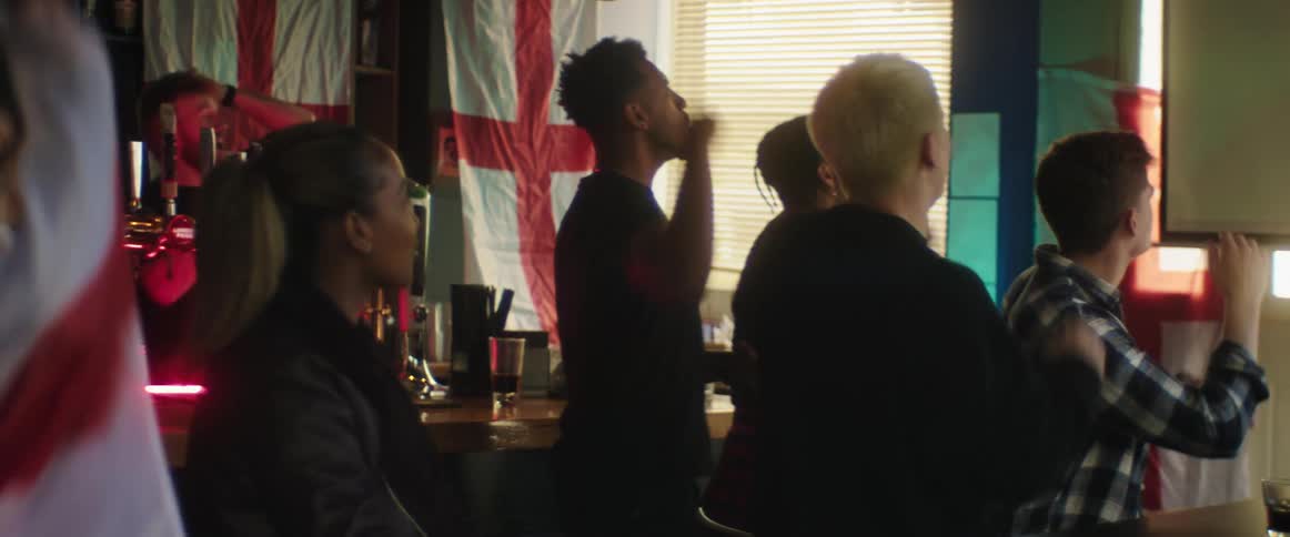 A group of people cheer while watching sports in a pub during the day