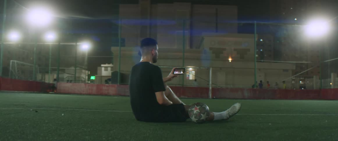 A man is sitting in a field looking at his cell phone and celebrating