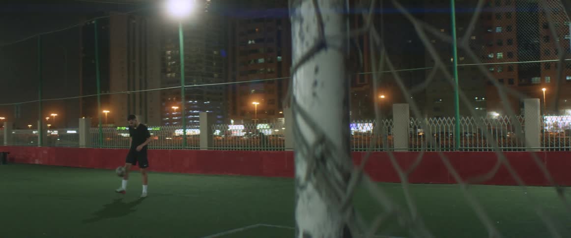 Young man practicing soccer on a soccer field in the city at night