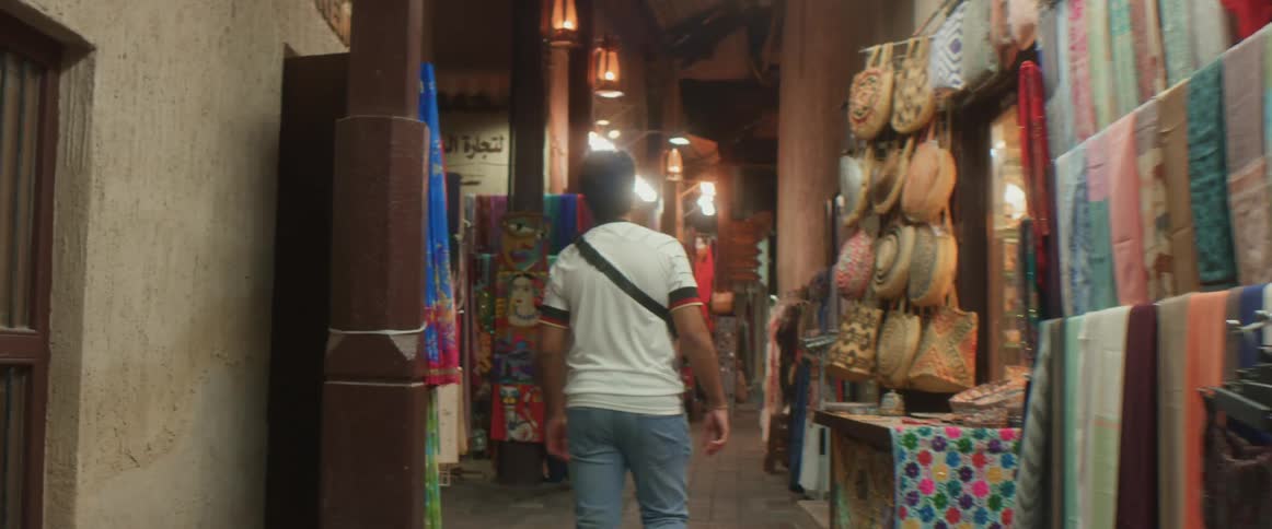A man walks through a market as an employee steps out of a shop