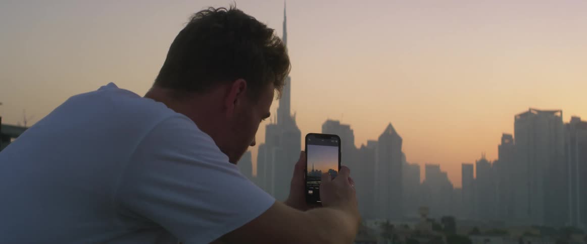 A man is taking pictures of a city skyline with his smart phone