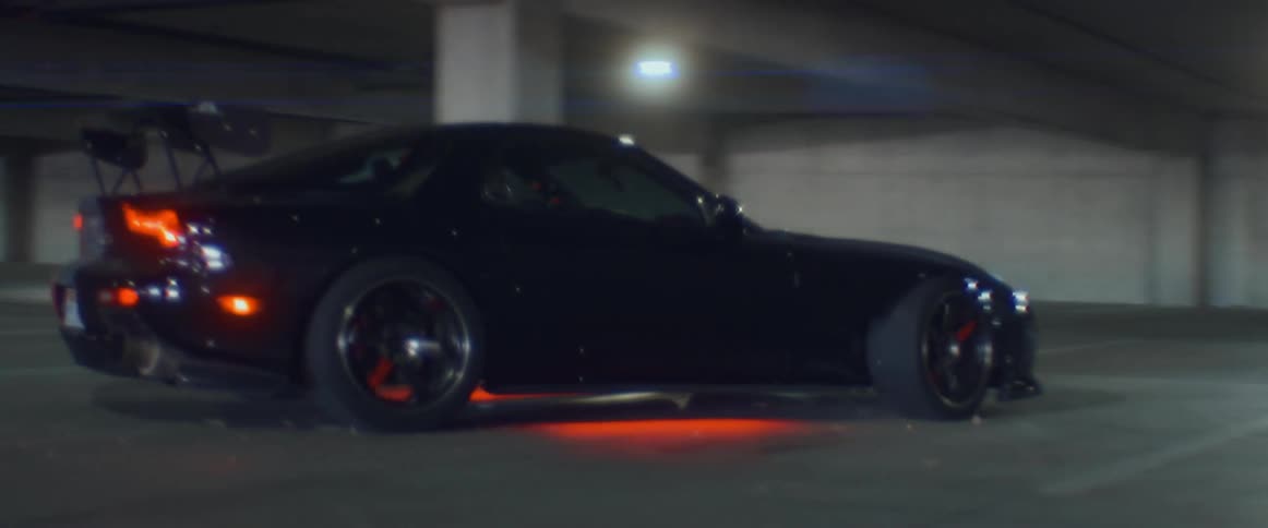 Black sports car with headlights on and red undercarriage lights parks inside a parking garage