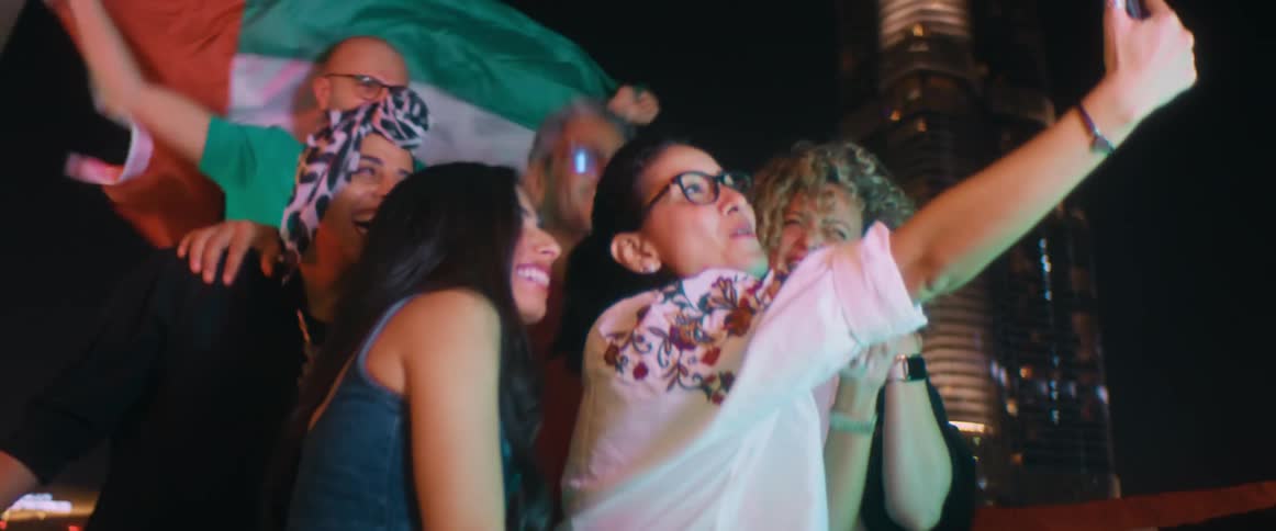 Group of happy friends celebrates jumping and waving flags while taking a selfie with a smartphone