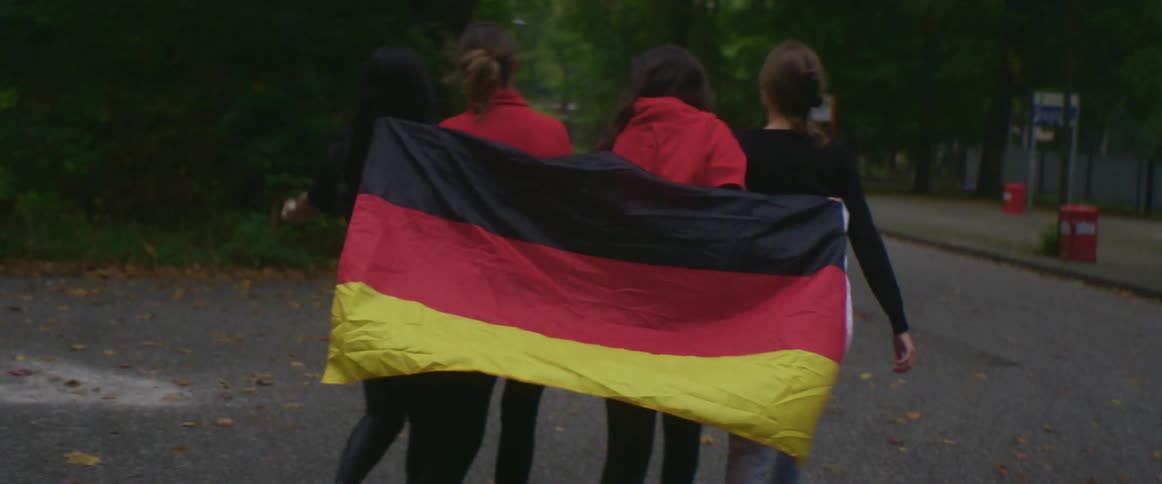 A group of female german football fans walks in the park carrying german flag