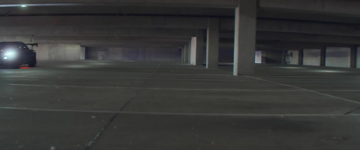 Black sports car with headlights on and red underglow lights parks on a parking garage
